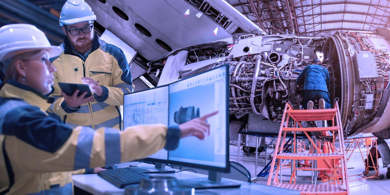 A mechanic works on an airplane engine while kneeling on an orange safety ladder. A male and a female engineer wearing yellow and black jackets and hardhats study plans on a computer monitor and tablet.